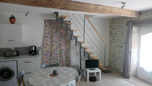 A compact kitchen with a washing machine, a toaster, and a coffee maker. A dining table with chairs is positioned near a staircase with a wooden handrail. - Duplex apartment very well located and quiet (Bretenoux)
