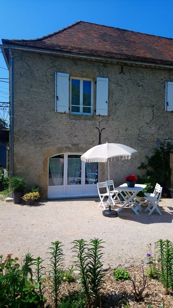 A house with a stone facade, a tiled roof, and a patio with outdoor furniture and a white umbrella.