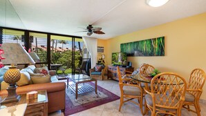 A well-lit living room with a glass coffee table, wicker chairs, a sofa, and a ceiling fan.