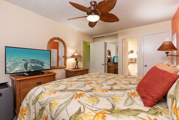 Habitación de hotel con cama, televisión, ventilador de techo, cómoda y baño visible a través de una puerta abierta.
