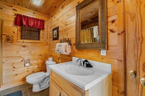 A wooden cabin bathroom with a white sink, toilet, and a mirror above the sink. - Caught Ya Peek'n 1 Bedroom Cabin by RedAwning (Pigeon Forge)