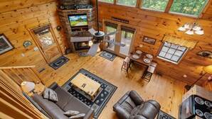 A cozy cabin interior with a fireplace, wooden walls, a sofa, a leather chair, and a dining area.