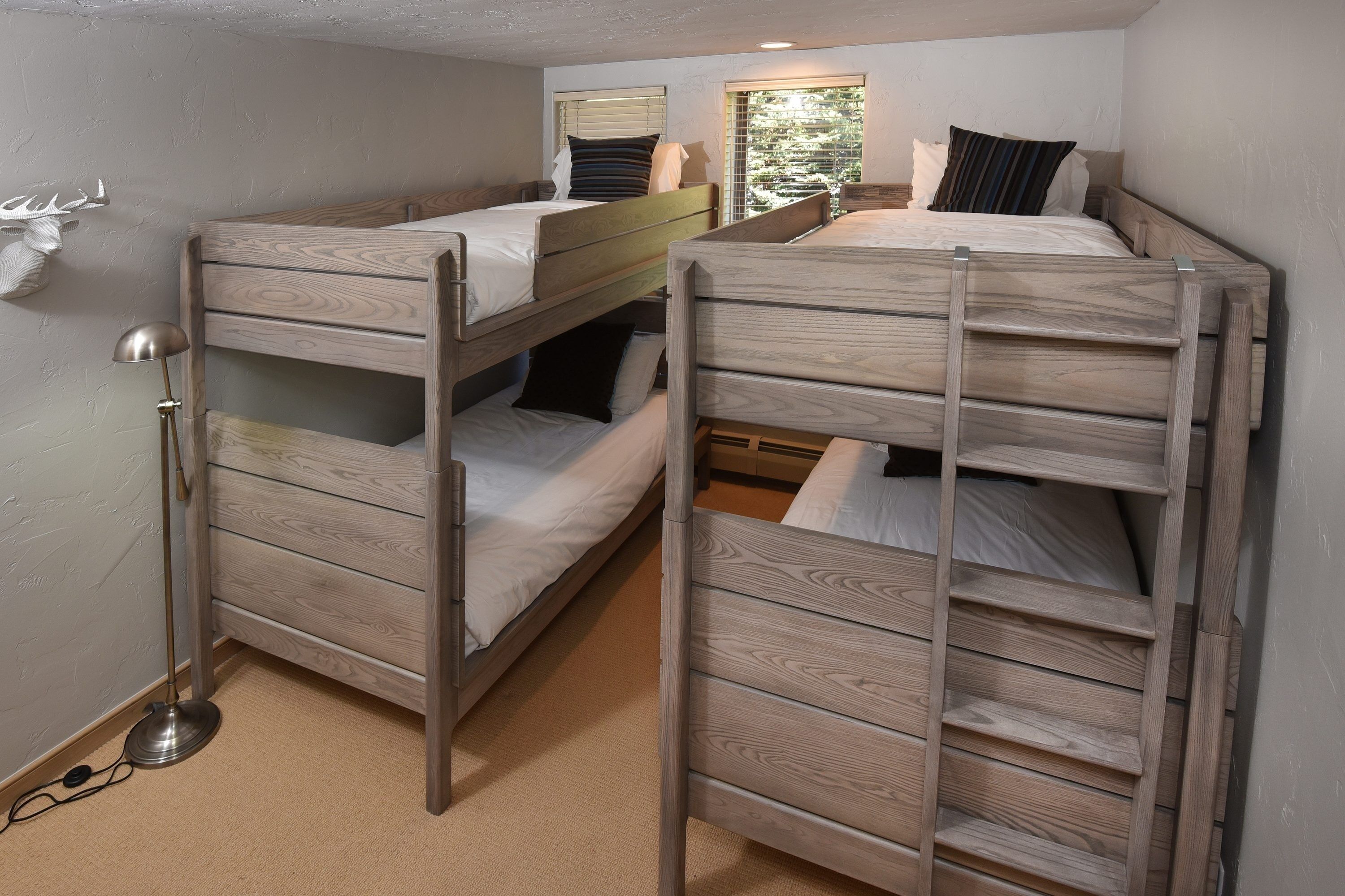 A dorm-style room with bunk beds, a lamp, and a window with blinds.