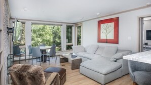 A modern living room with a grey sectional sofa, a fur chair, and a dining area with a glass table and chairs. - Gateway Plaza R4 2 Bedroom Condo by RedAwning (Vail)
