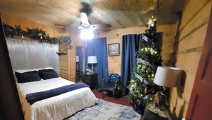 A bedroom with a bed, a nightstand, a lamp, a Christmas tree, and a ceiling fan.