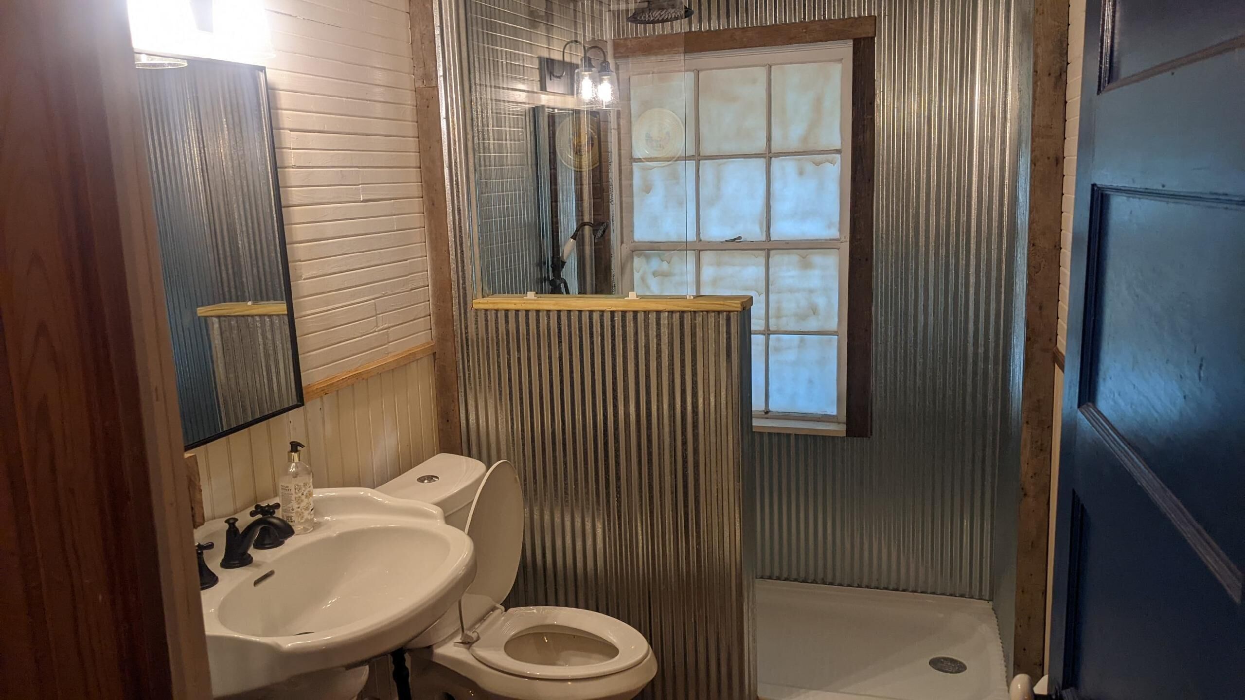 A bathroom with a sink, toilet, shower, and a window.