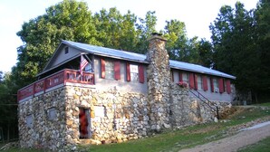A stone building with a metal roof, a flagpole with an American flag, and a gravel driveway.