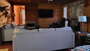 A cozy living room with a white sofa, a television, a fireplace, and a window with a view of the outdoors.