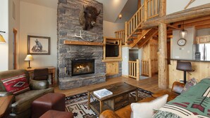 Un interior rústico con chimenea de piedra, muebles de cuero y una escalera de madera.