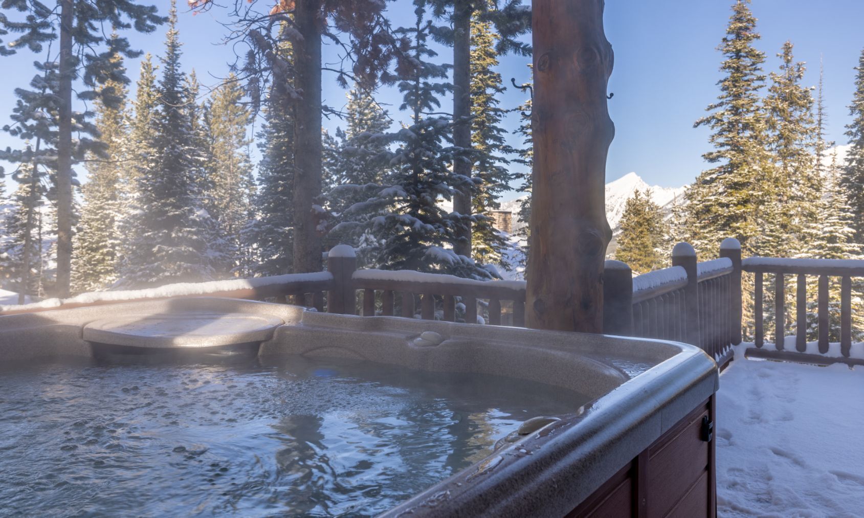 A hot tub surrounded by snow-covered trees and a wooden deck.