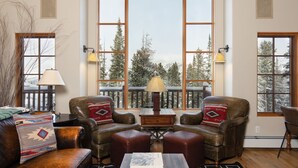 Una sala de estar acogedora con muebles de cuero, ventanas amplias con vistas a árboles y un balcón con barandilla.