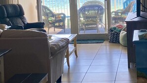 Ein Wohnzimmer mit einer Couch, einem Couchtisch und einem Fernsehschrank. Eine Glastür führt auf einen Balkon mit Blick aufs Meer.