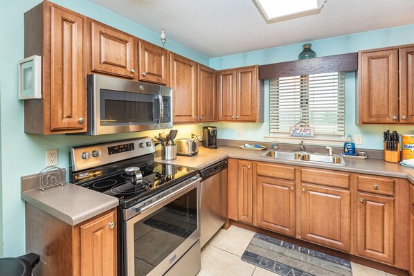 A kitchen with wooden cabinets, stainless steel appliances, and a window with blinds.
