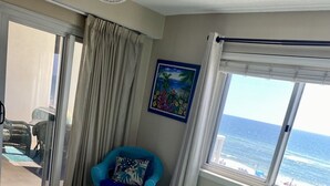 Ein Hotelzimmer mit einem großen Bett, Meerblick, einem Sessel und einem Bild an der Wand.