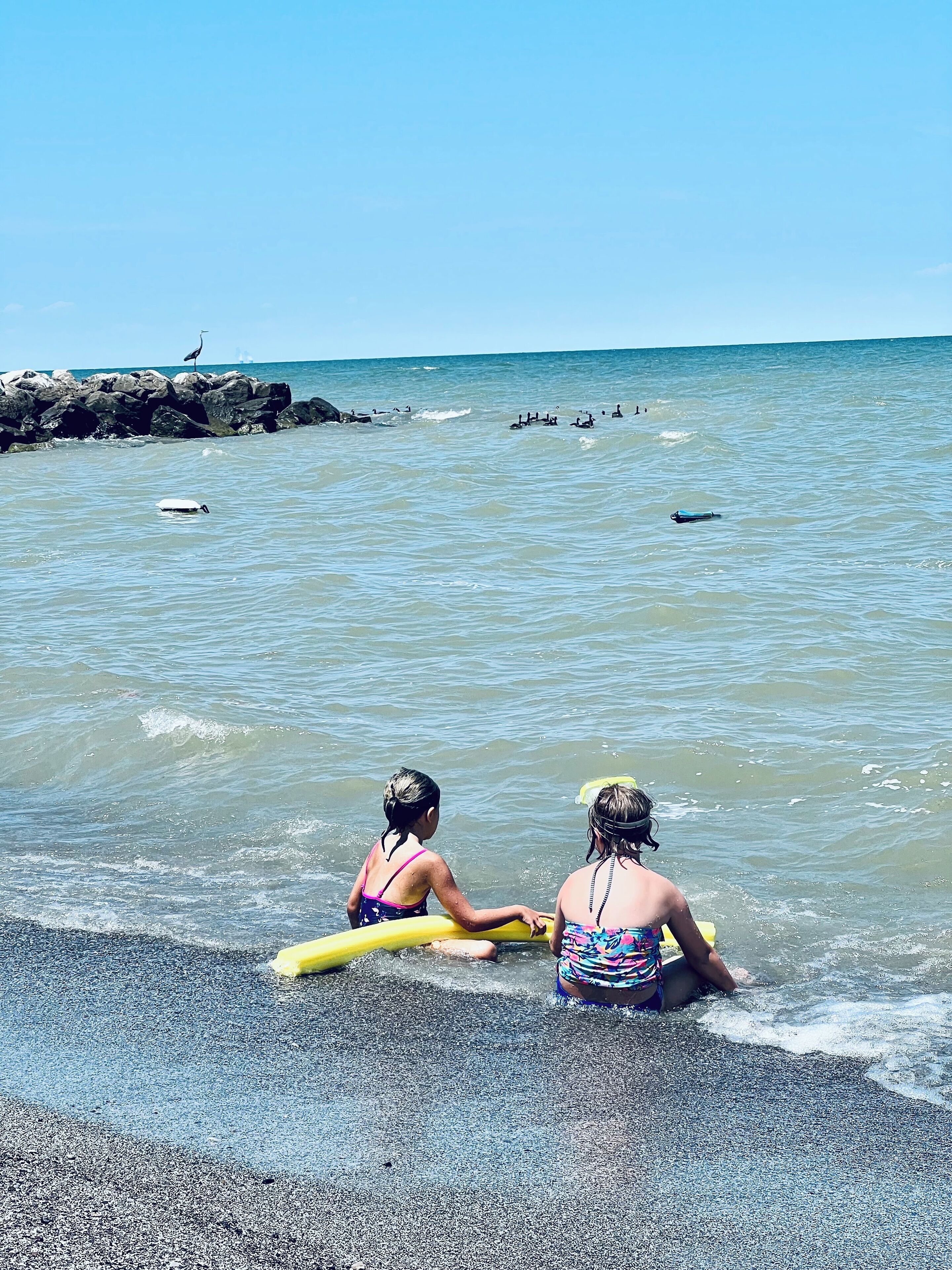 Två personer på en strand med en stenig kust och ett lugnt hav.