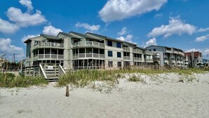 Et hotel ved stranden med flere balkoner og en sandstrand i forgrunden.
