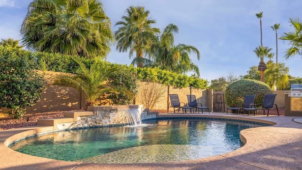 A pool with a waterfall feature, surrounded by palm trees and lounge chairs. - Family Home with Pool, Hot Tub & BBQ near Kierland (Scottsdale)