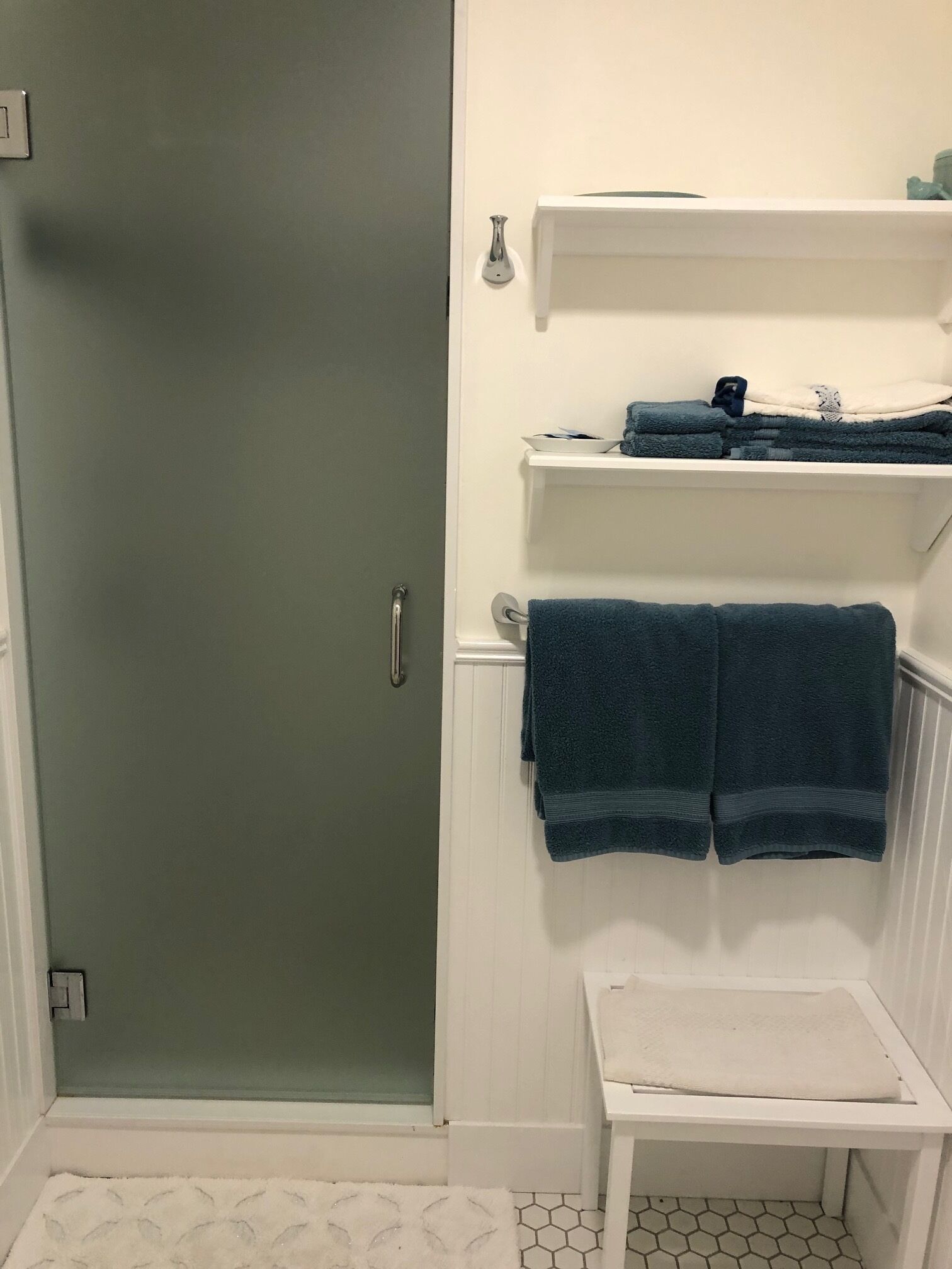 A bathroom with a shower, a white sink, and a towel rack with folded towels.