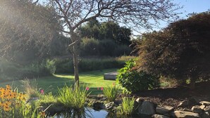 A serene garden with a pond, lush greenery, and a golf course in the background. - Next Door to Golf Course, Minutes to Beaches! (Middletown)