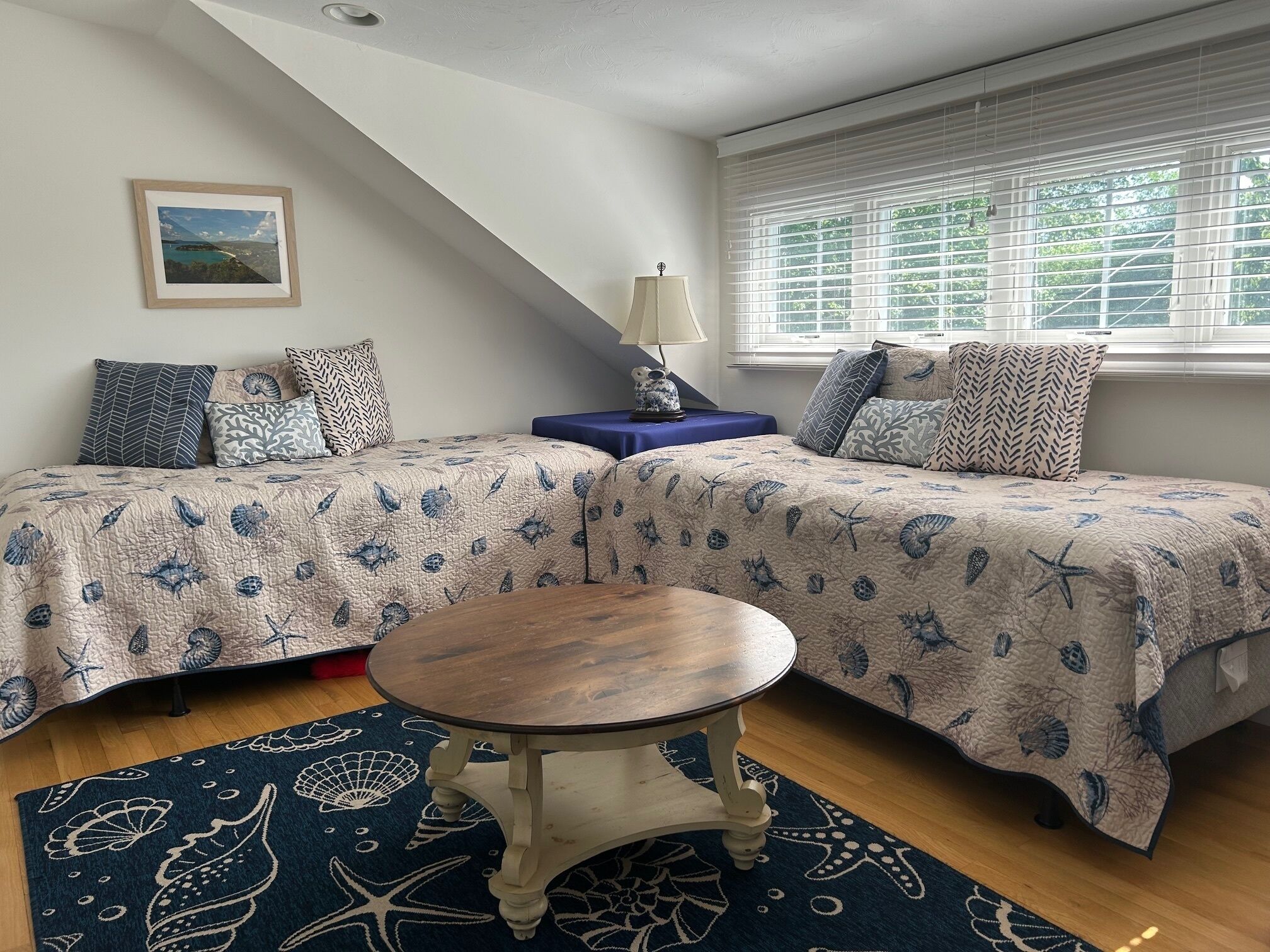 Une chambre avec deux lits, une petite table ronde, une lampe et une fenêtre avec des stores.