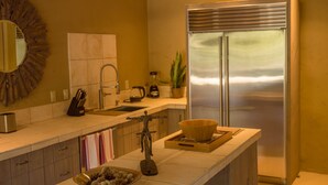 A modern kitchen with a stainless steel refrigerator, a sink, and a countertop with a bowl and a small statue. - Forest Opulence: Center of PB Resorts: Four Seasons Beds (Del Monte Forest)