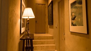 A hallway with a lamp, framed pictures, and a staircase leading to a door. - Forest Opulence: Center of PB Resorts: Four Seasons Beds (Del Monte Forest)