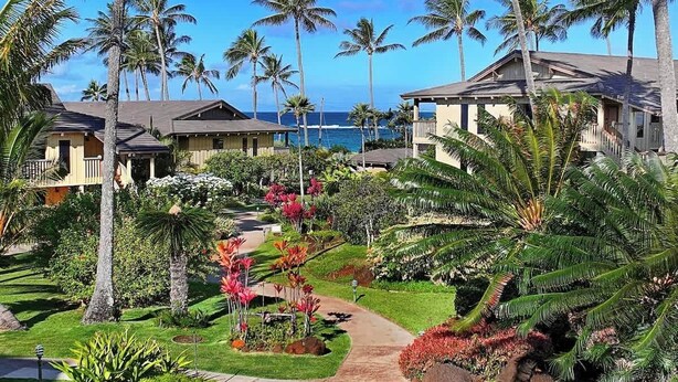 Un complexe hôtelier comprenant plusieurs bâtiments de style bungalow, un jardin bien entretenu avec des plantes tropicales et une vue sur l’océan.