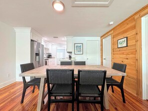 Una cocina moderna con armarios blancos, un refrigerador de acero inoxidable y un comedor con mesa de madera y sillas negras.