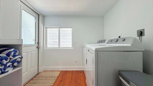 A laundry room with a washing machine, dryer, and a door leading to a hallway. - 231 Pearl Island Cottage Retreat w Private Pool (Fort Myers Beach)