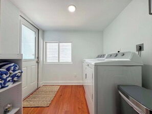 A laundry room with a washing machine, dryer, and a door leading to a hallway. - 231 Pearl Island Cottage Retreat w Private Pool (Fort Myers Beach)