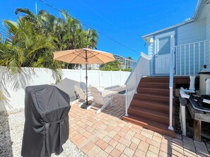 A covered outdoor seating area with a grill, a covered barbecue, and a staircase leading to a house.