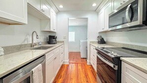 A compact kitchen with white cabinetry, a built-in microwave, and a coffee maker. - 231 Pearl Island Cottage Retreat w Private Pool (Fort Myers Beach)