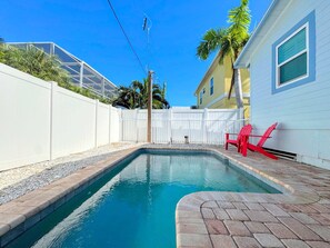 Una piscina con una cerca blanca, una silla roja y un edificio con ventana.
