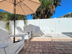 A patio area with Adirondack chairs, a table, and a beige umbrella. - 231 Pearl Island Cottage Retreat w Private Pool (Fort Myers Beach)