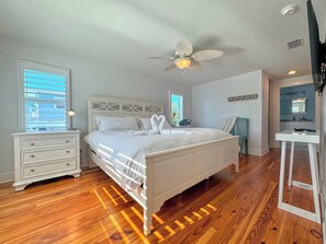 A bedroom with a bed, a nightstand, a dresser, a ceiling fan, and a bathroom with a mirror and sink.