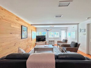 A living room with a wooden wall, a television, a sofa, and a coffee table. - 231 Pearl Island Cottage Retreat w Private Pool (Fort Myers Beach)