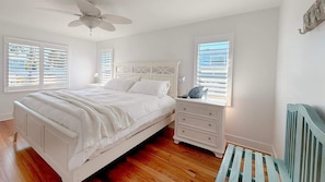 A bedroom with a bed, nightstands, a dresser, a ceiling fan, and windows with blinds. - 231 Pearl Island Cottage Retreat w Private Pool (Fort Myers Beach)