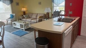 Un espace de vie compact comprenant un coin cuisine, un canapé, une table à manger et une petite poubelle.