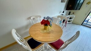 Un coin repas avec une table ronde en bois, des chaises blanches avec des coussins et un vase rempli de fleurs rouges.
