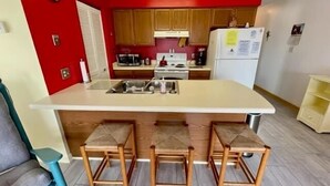 Une cuisine compacte dotée d’un îlot central, de tabourets en bois et d’appareils électroménagers de base.