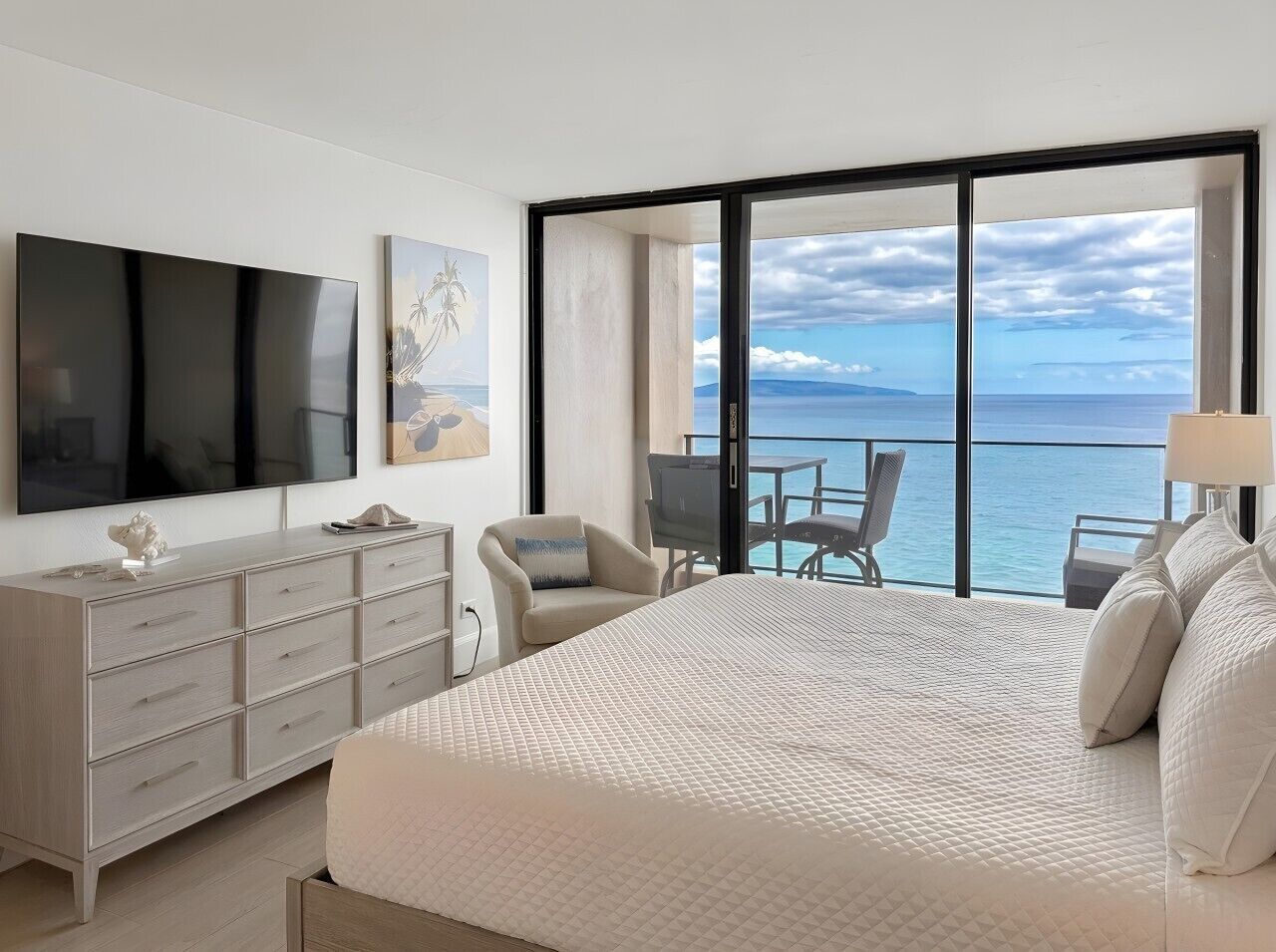 Une chambre d’hôtel avec un grand lit, une télévision, un bureau avec une chaise et un balcon donnant sur la mer.