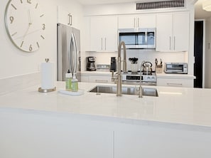 A modern kitchen with white cabinetry, stainless steel appliances, and a large wall clock.