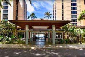 A hotel entrance with a covered walkway, palm trees, and a view of the ocean.