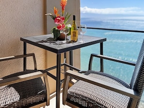 A balcony with a table, two chairs, a bottle of wine, and a glass.
