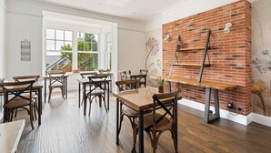 Un comedor con mesas y sillas de madera, una pared de acento de ladrillo y un ventanal con vistas a la vegetación.