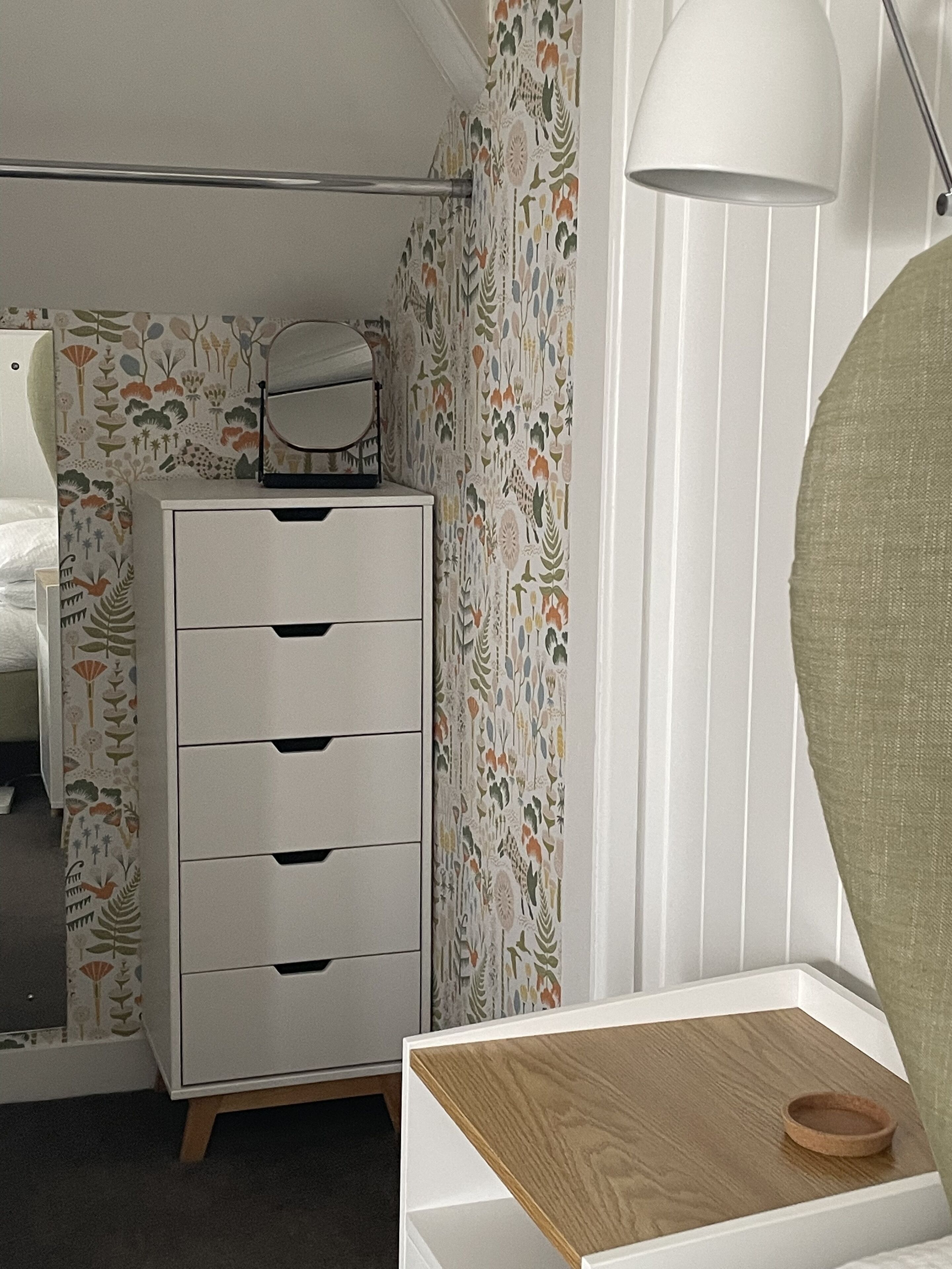 A bedroom with a white dresser, a mirror, and a wooden side table.