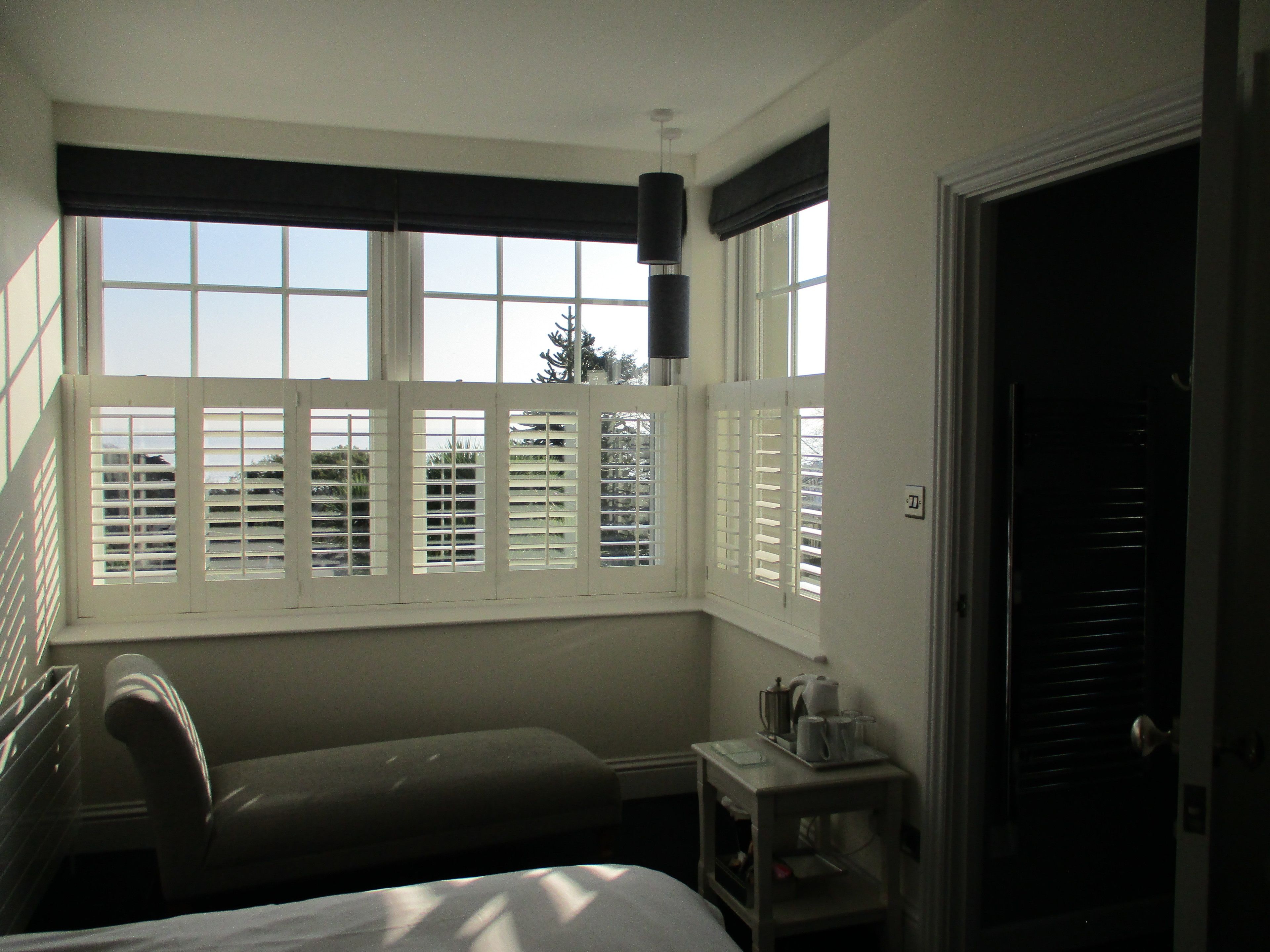 A hotel room with a bed, a small table with a lamp, and a window with blinds.