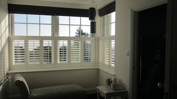 A hotel room with a bed, a small table with a lamp, and a window with blinds.