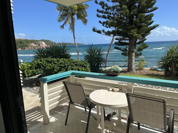 A balcony with a view of the ocean, a table, chairs, and a potted plant.