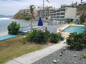 Un espace piscine offrant une vue sur l’océan, entouré de verdure et bordé d’un immeuble doté de nombreux balcons.